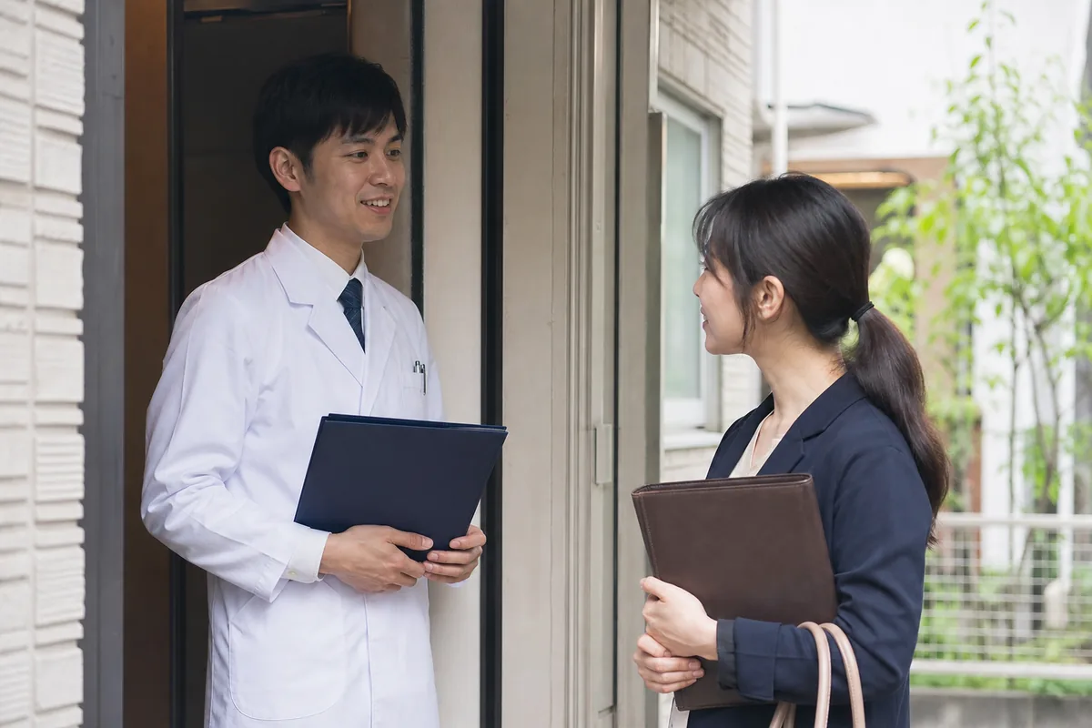患者宅の玄関先で打ち合わせる薬剤師とケアマネジャー