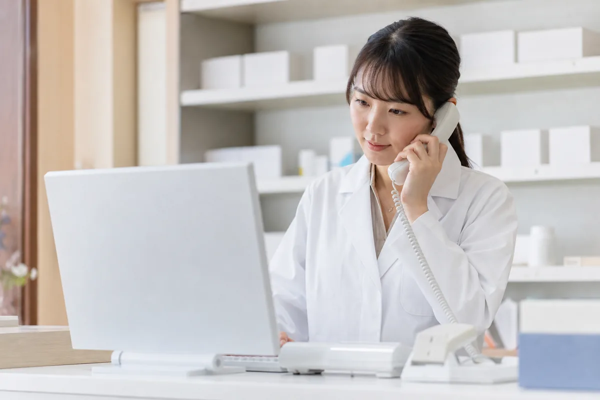 薬局のカウンターで電話フォローを行う薬剤師